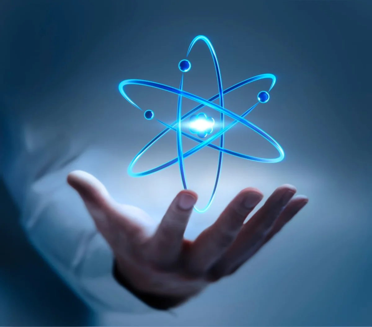 Glowing blue atom graphic hovering above an open human hand against a dark blue background