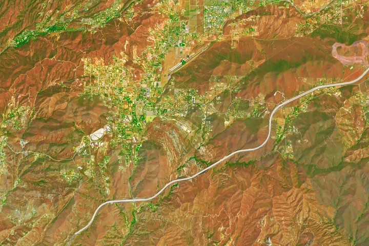 Satellite view shows rust-colored rugged terrain, green valleys, settlements, and a winding highway.