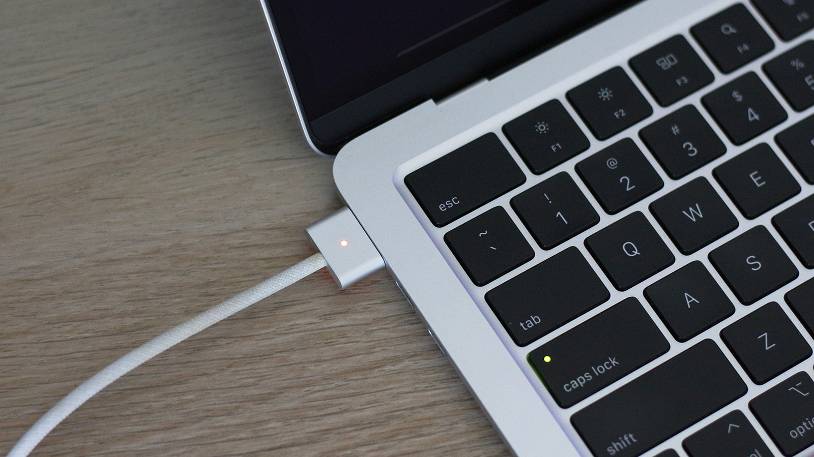 Close-up of a laptop keyboard with a white magnetic charging cable connected on a wooden desk