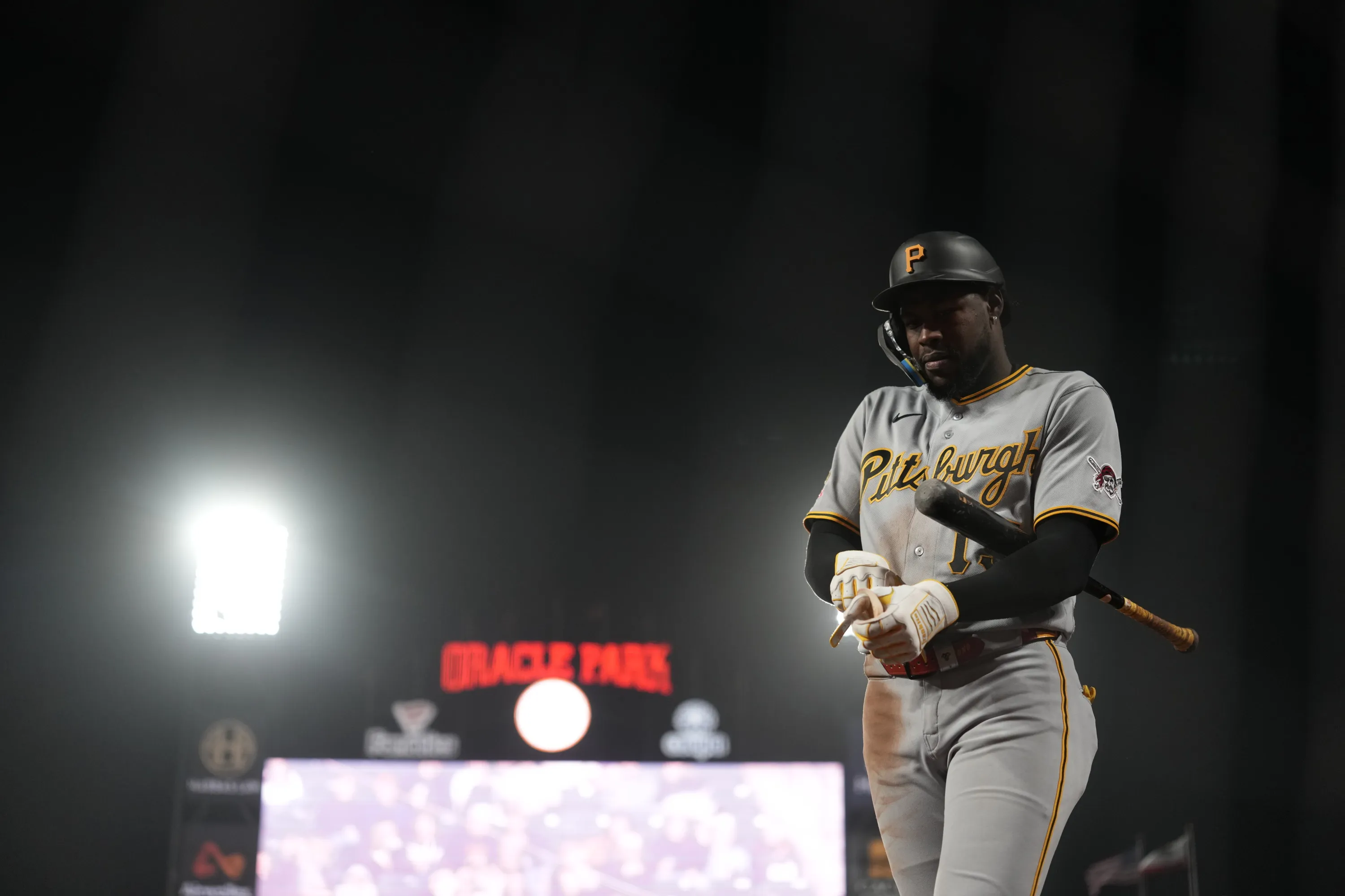 Baseball player in a Pittsburgh uniform holds a bat beneath bright stadium lights.