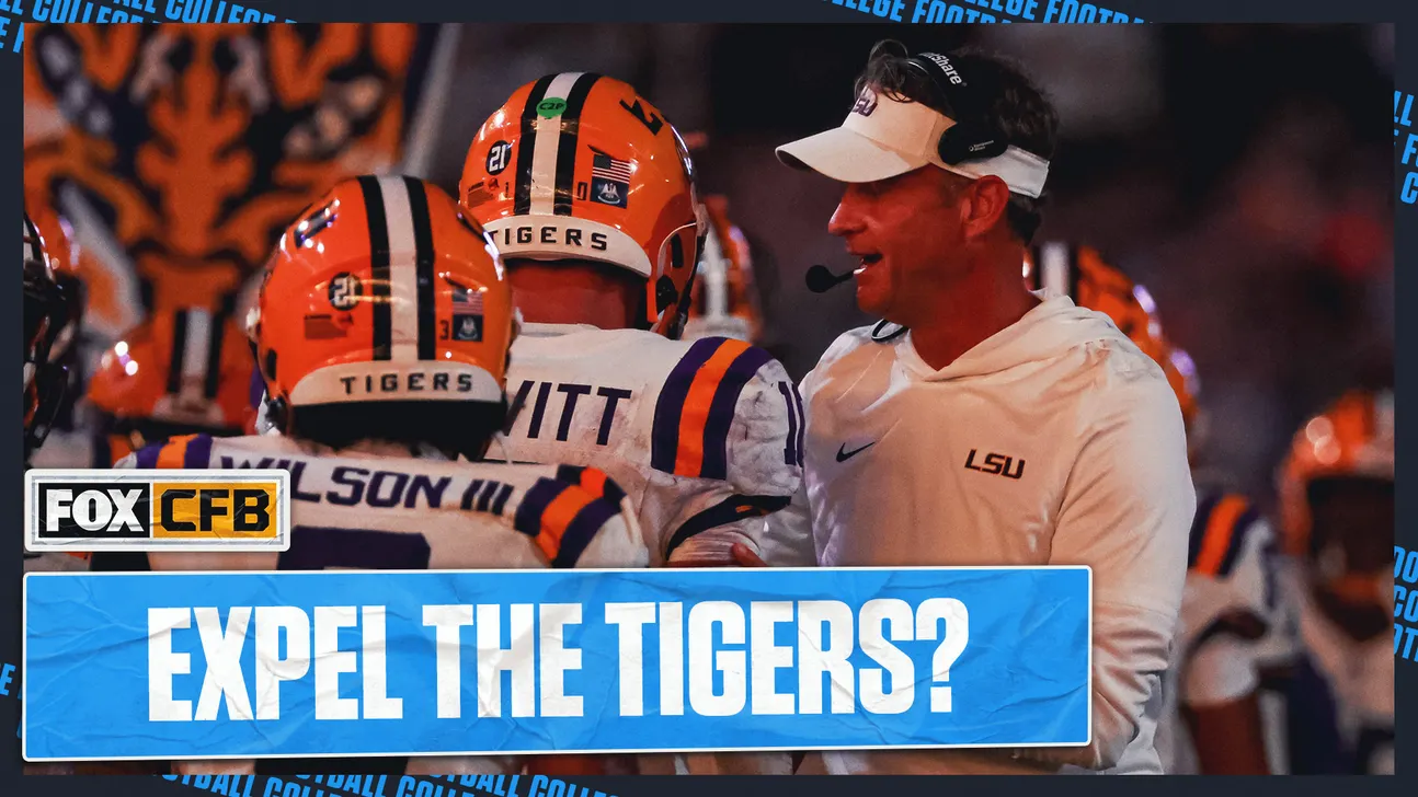LSU football players and coach huddle during a game amid a crowded stadium backdrop