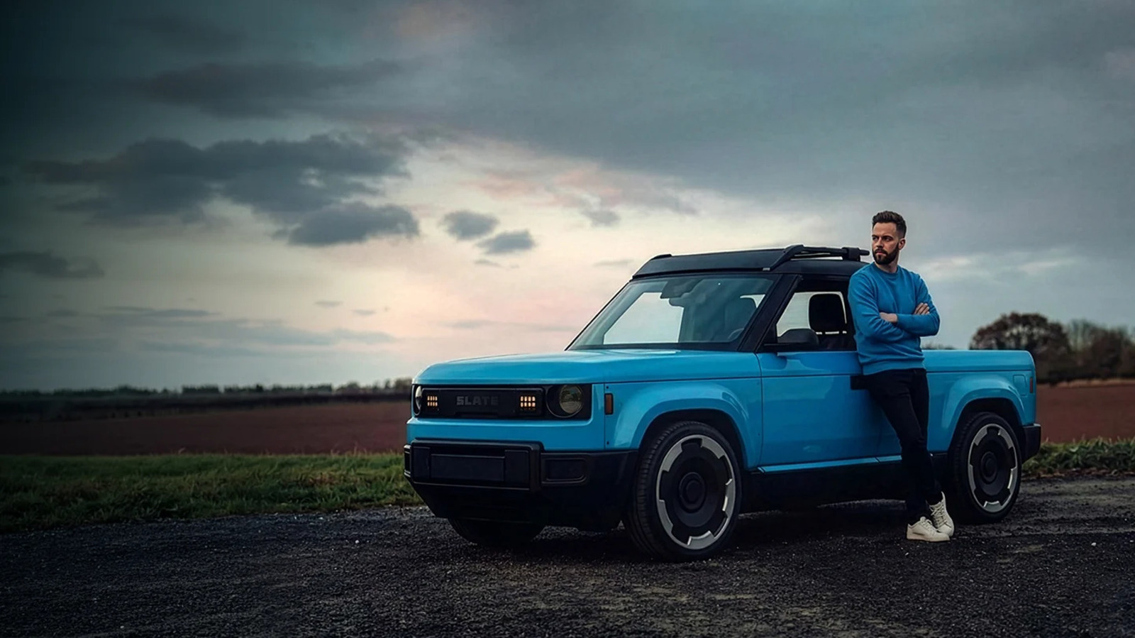 Blue Slate electric pickup truck parked on a rural road with a man standing beside it