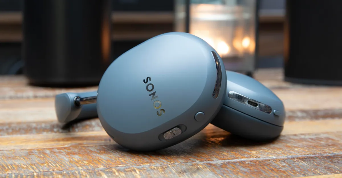 Blue Sonos over-ear headphones rest on a wooden surface, one earcup facing forward.