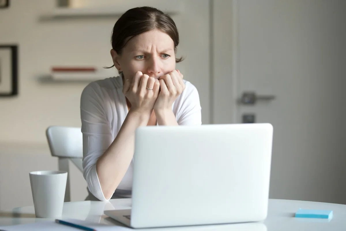 Worried woman biting her nails while sitting behind a laptop at a table
