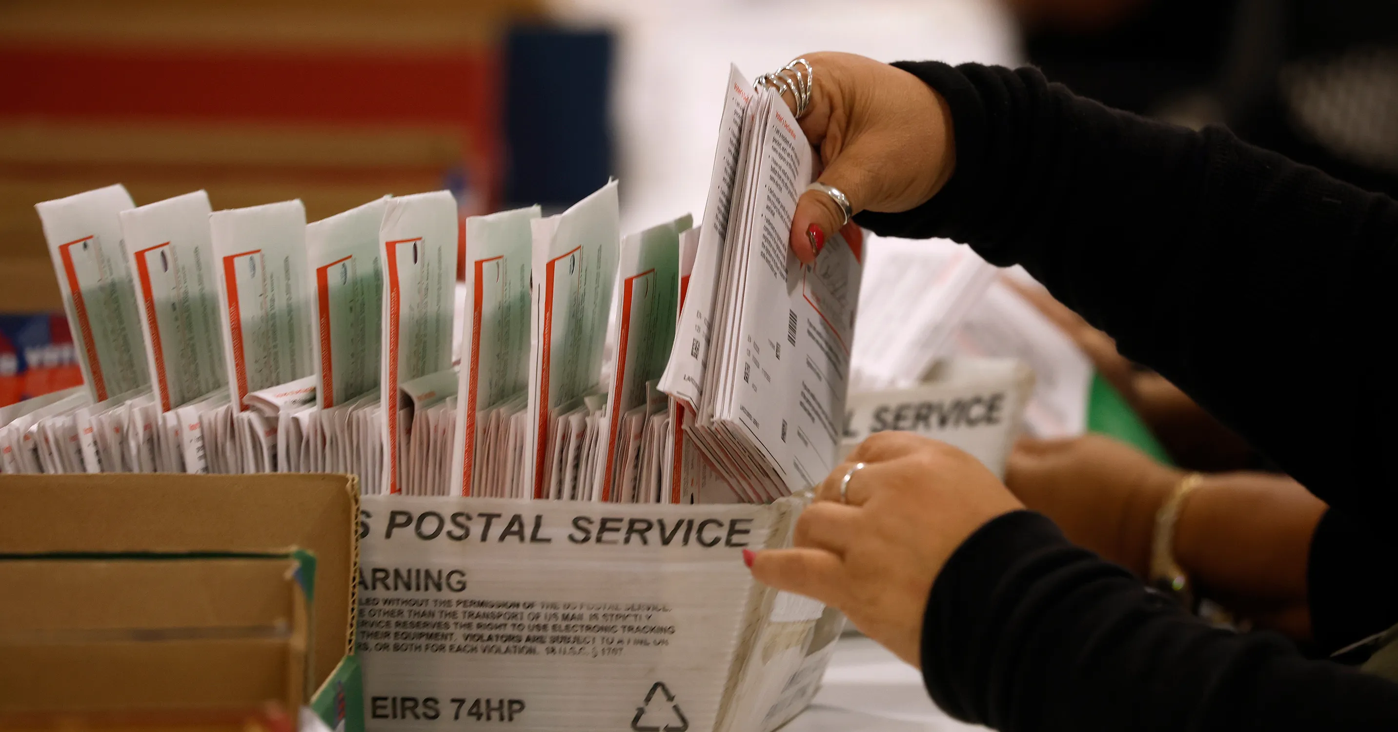Person sorts stacks of envelopes in United States Postal Service containers
