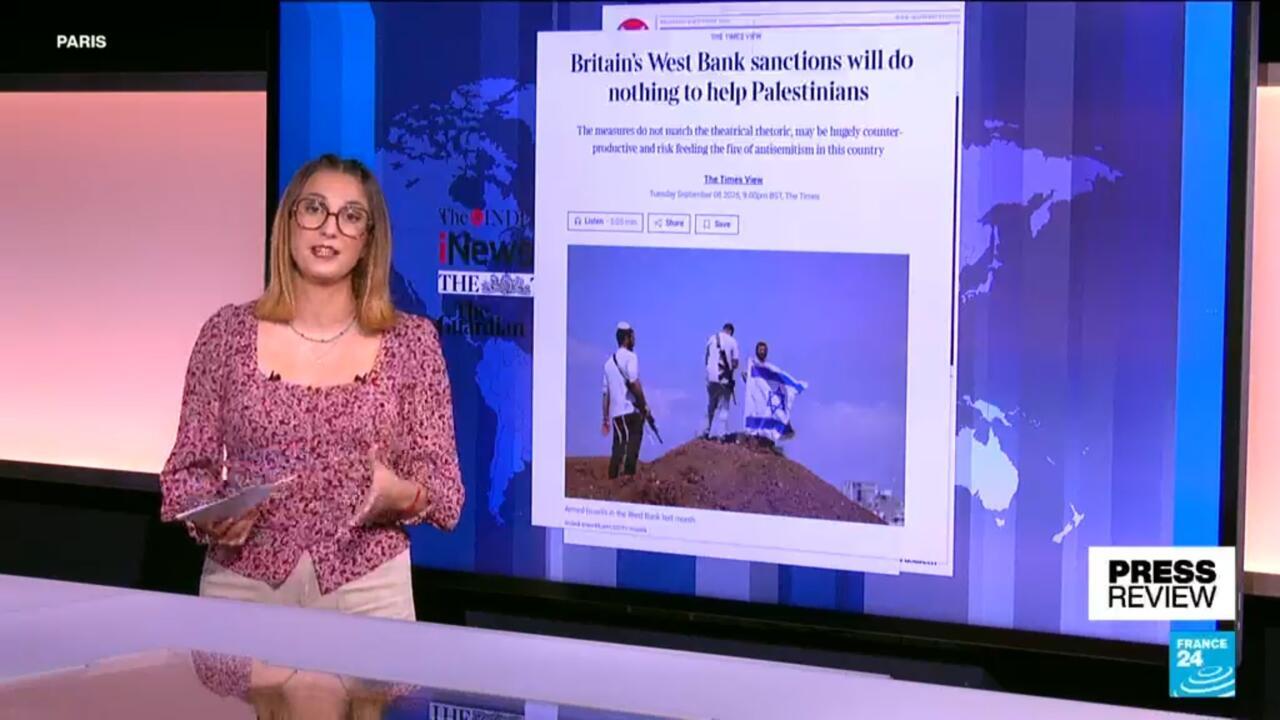 News presenter stands beside a screen displaying a Times article about sanctions on Israel.
