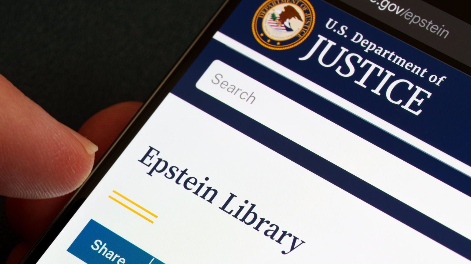 A hand holds a phone displaying the U.S. Department of Justice website and an Epstein Library page.