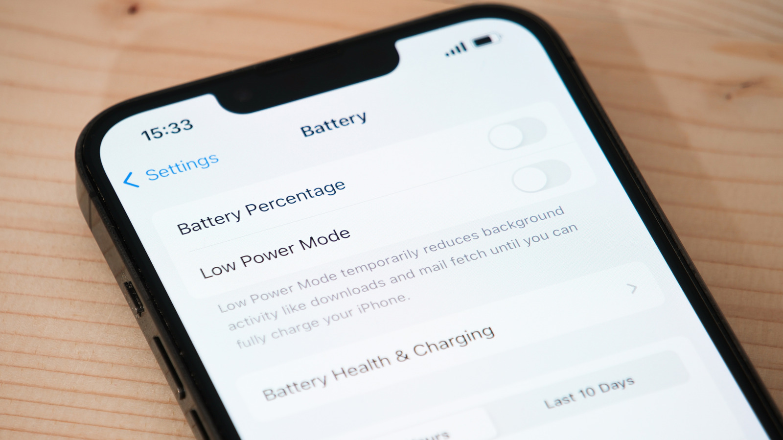 Close-up of an iPhone on a wooden surface displaying Battery settings with Battery Percentage and Low Power Mode switches.
