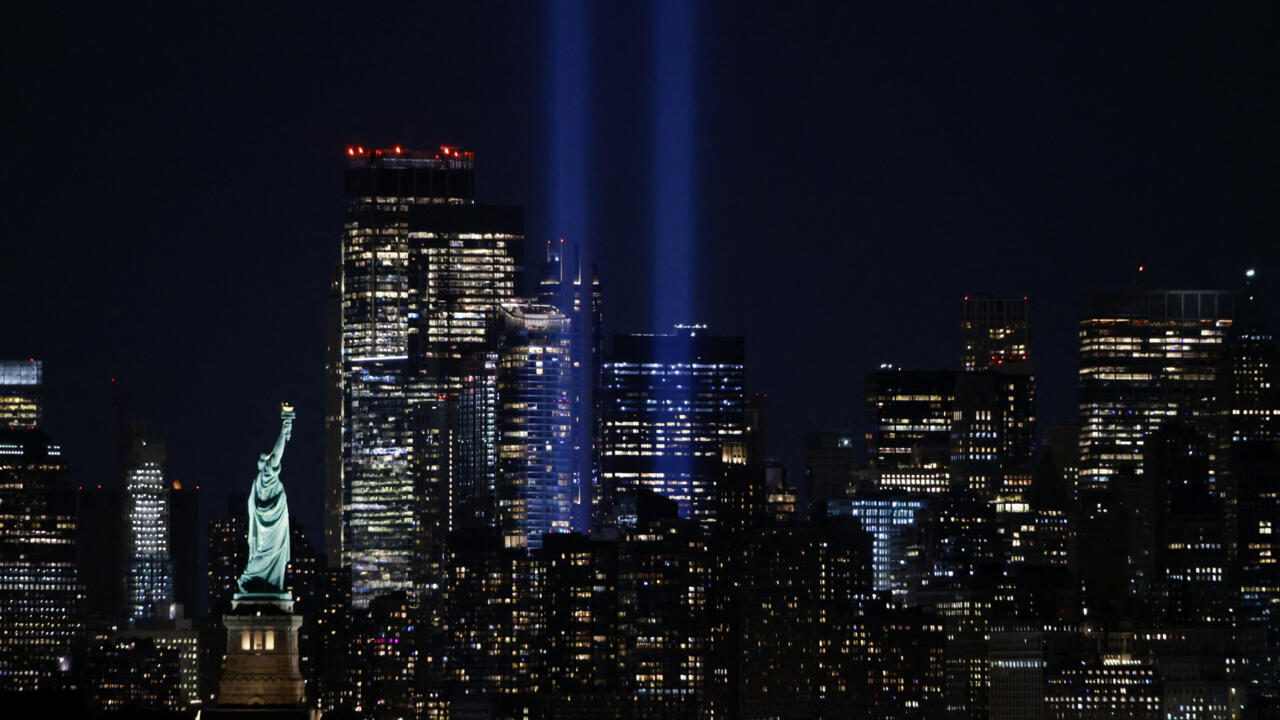 Nighttime city skyline with illuminated skyscrapers and a replica Statue of Liberty in foreground