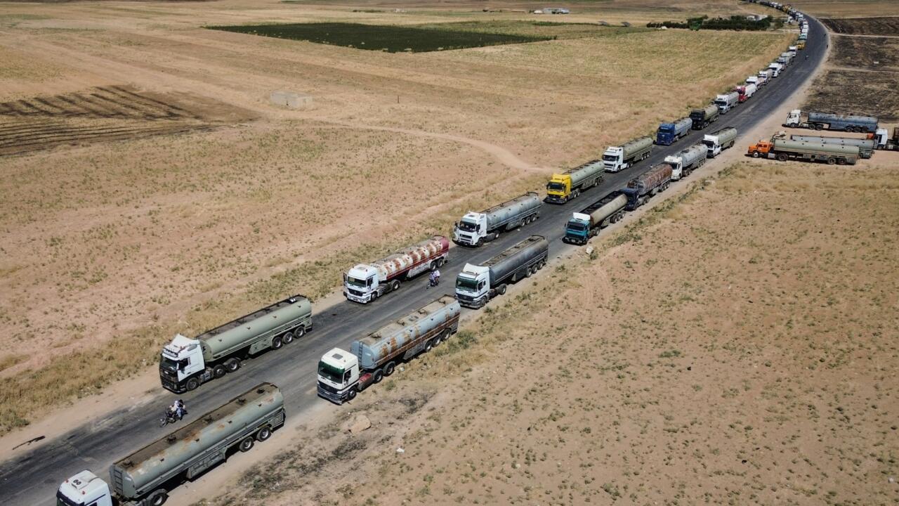 Aerial view of tanker trucks queued along a road crossing a dry, sparsely vegetated landscape.