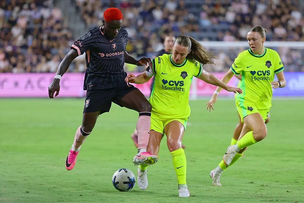 Three soccer players contest the ball during a match, with two wearing neon yellow kits.