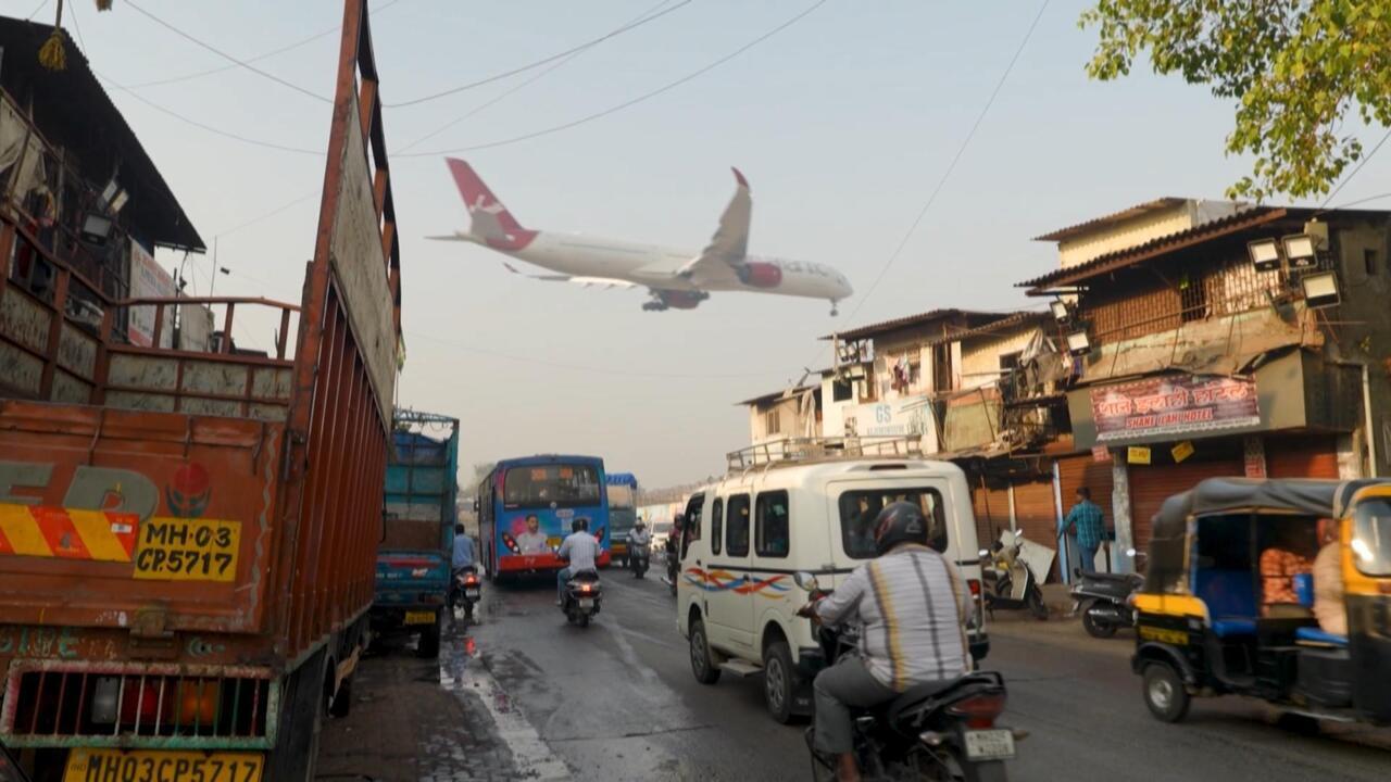 Passenger airplane flying low over a congested urban street filled with buses, cars, motorcycles and auto-rickshaws.
