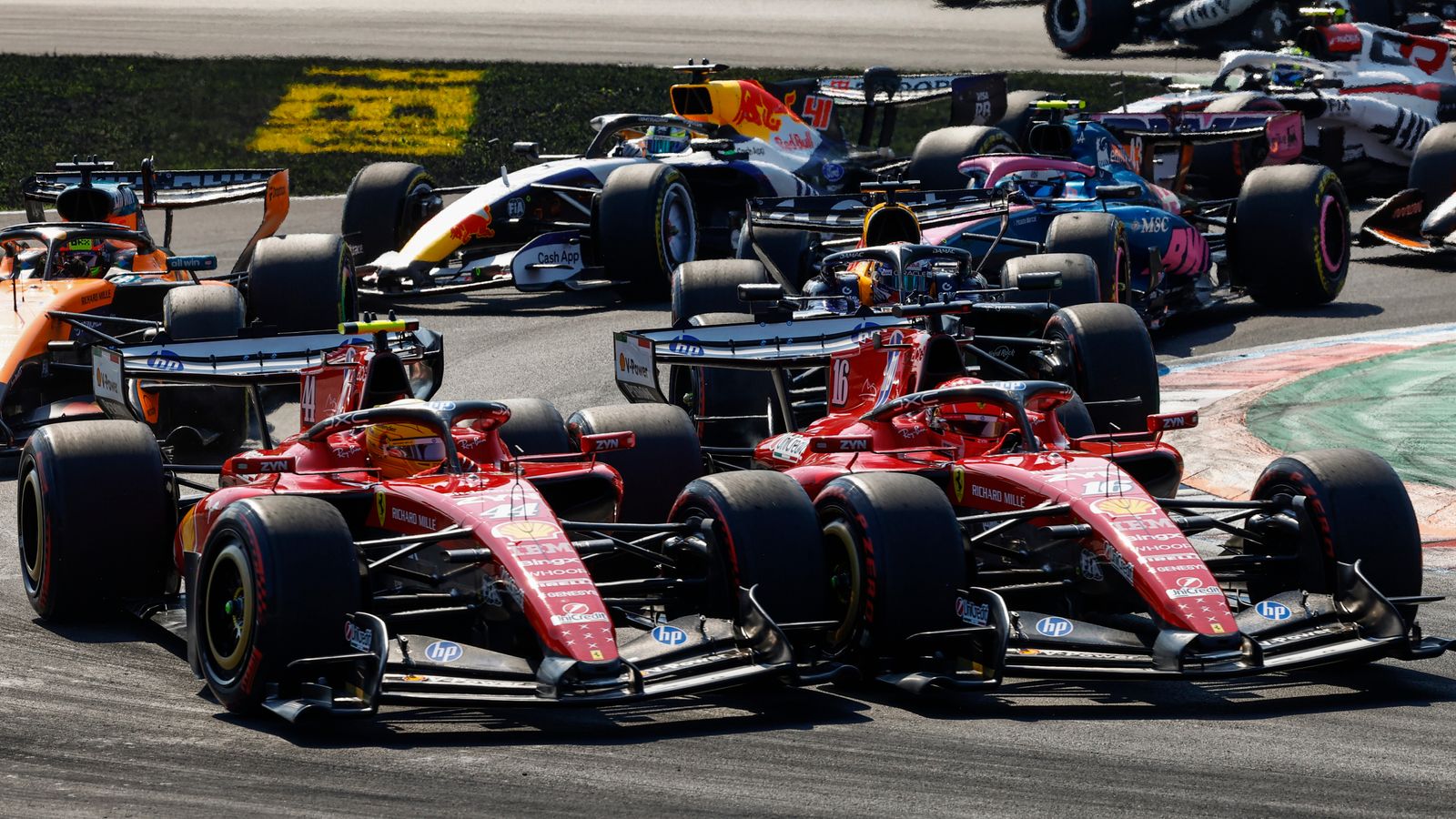 Several Formula 1 cars race closely together, with two red cars leading through a corner.