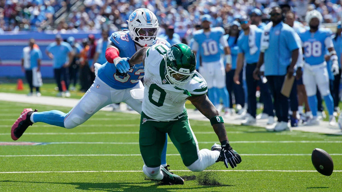 New York Jets player runs as a Tennessee Titans defender pursues a loose football