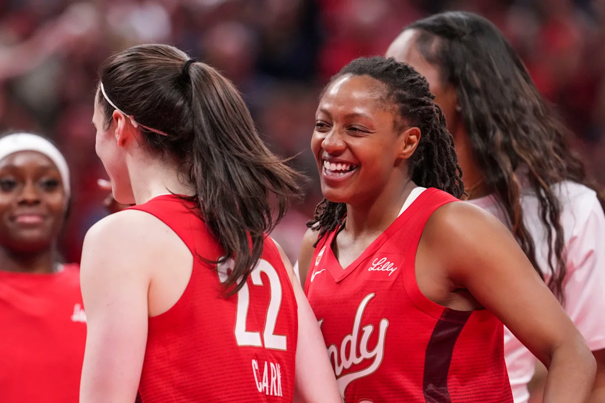 Two basketball players in red uniforms smile and talk during a game.