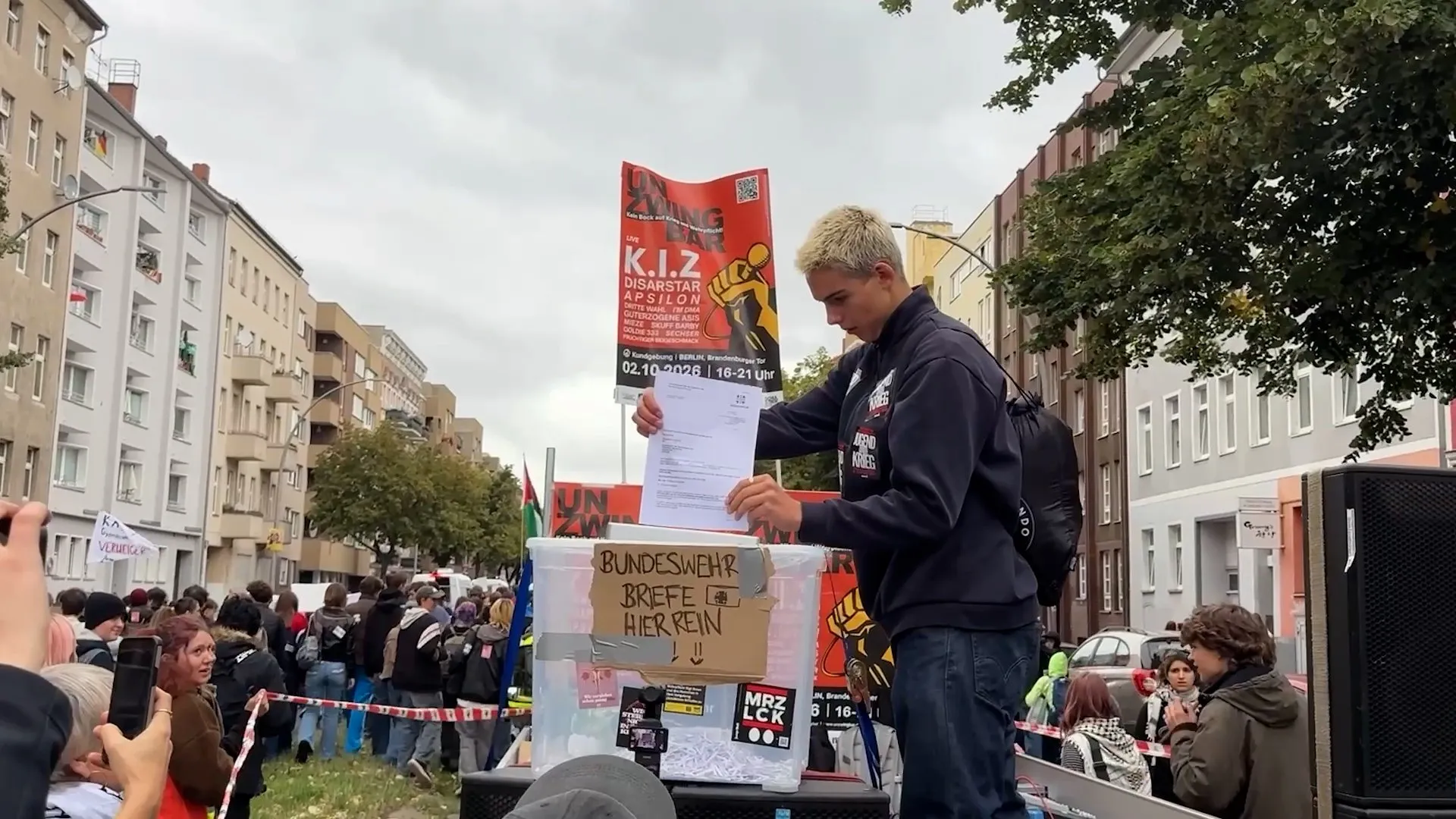 A young person places a paper into a box labeled for Bundeswehr letters at a street protest.