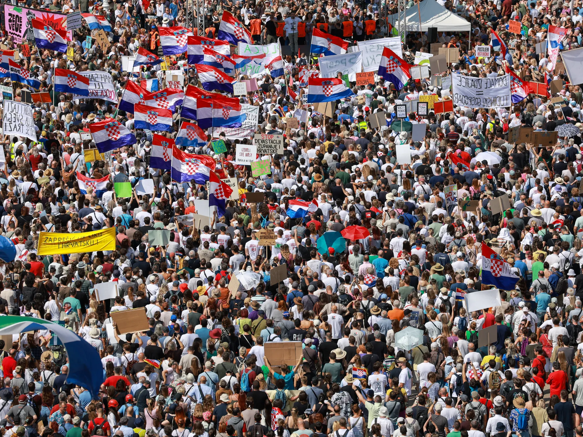 Large crowd holds Croatian flags and protest signs during a densely packed outdoor demonstration