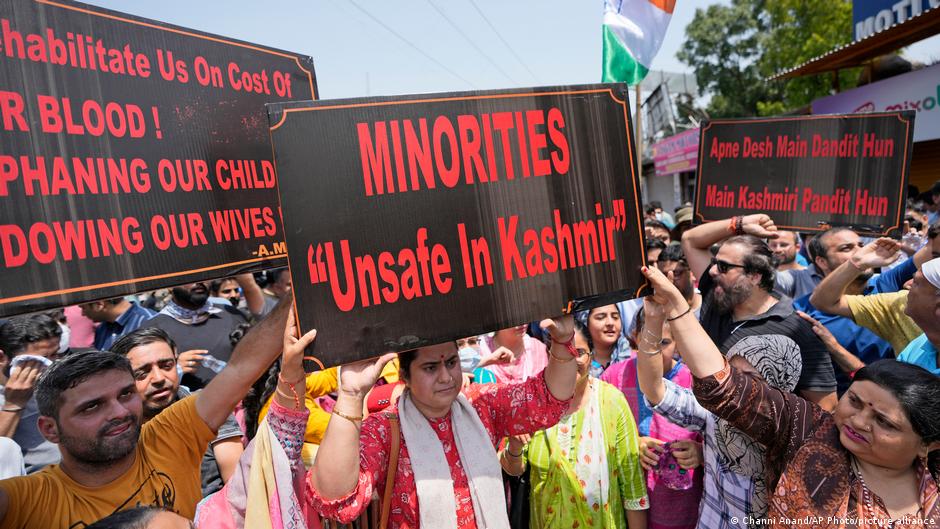 Protesters hold signs expressing fears about minority safety and Kashmiri Pandit security.