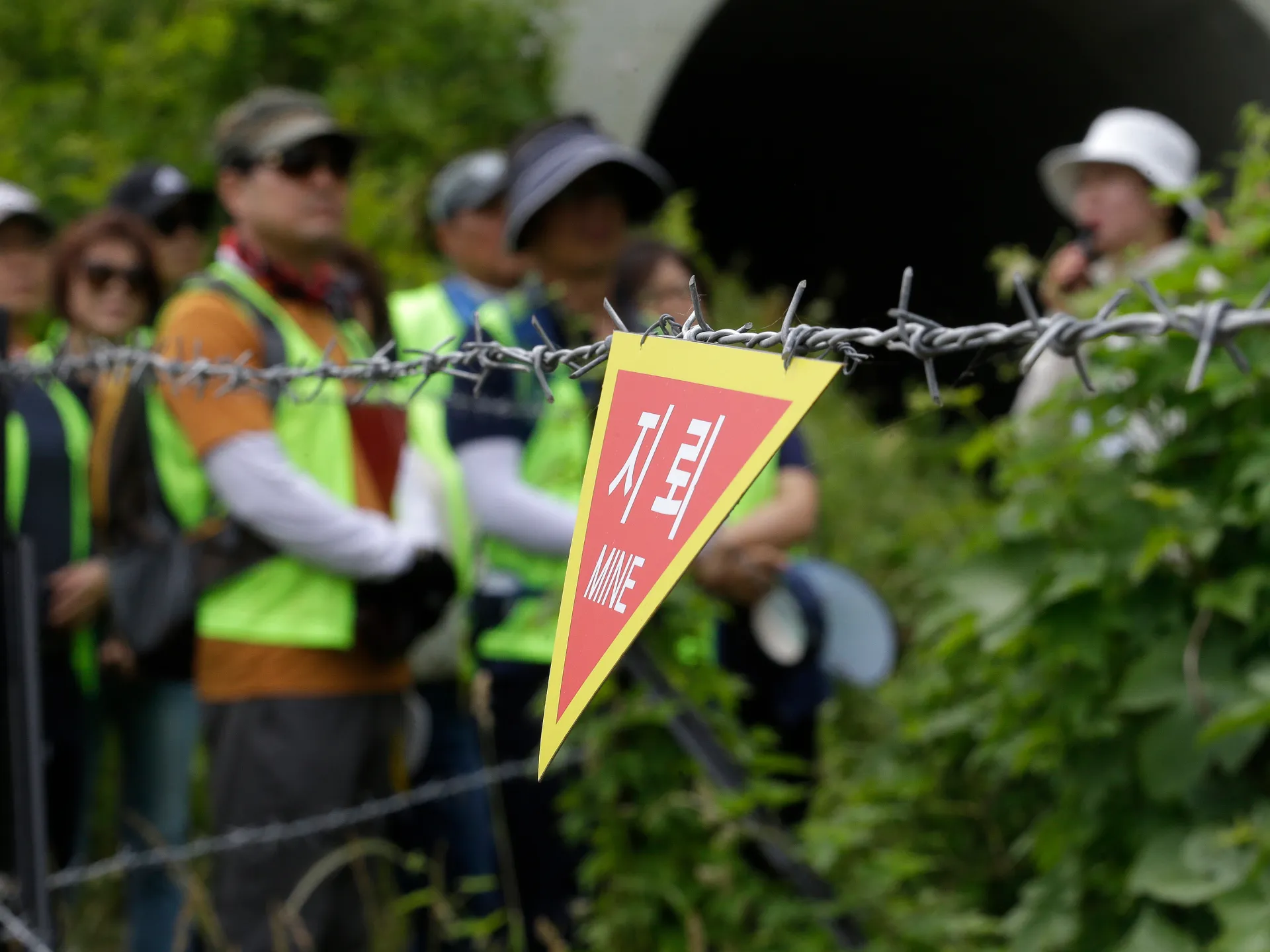 Warning sign attached to barbed wire with blurred people and forested background