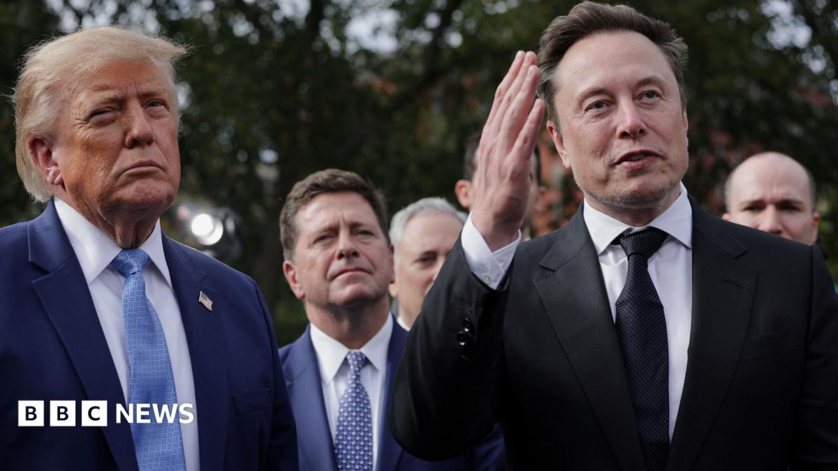 Donald Trump stands beside Elon Musk, who raises one hand, with several men behind them outdoors.