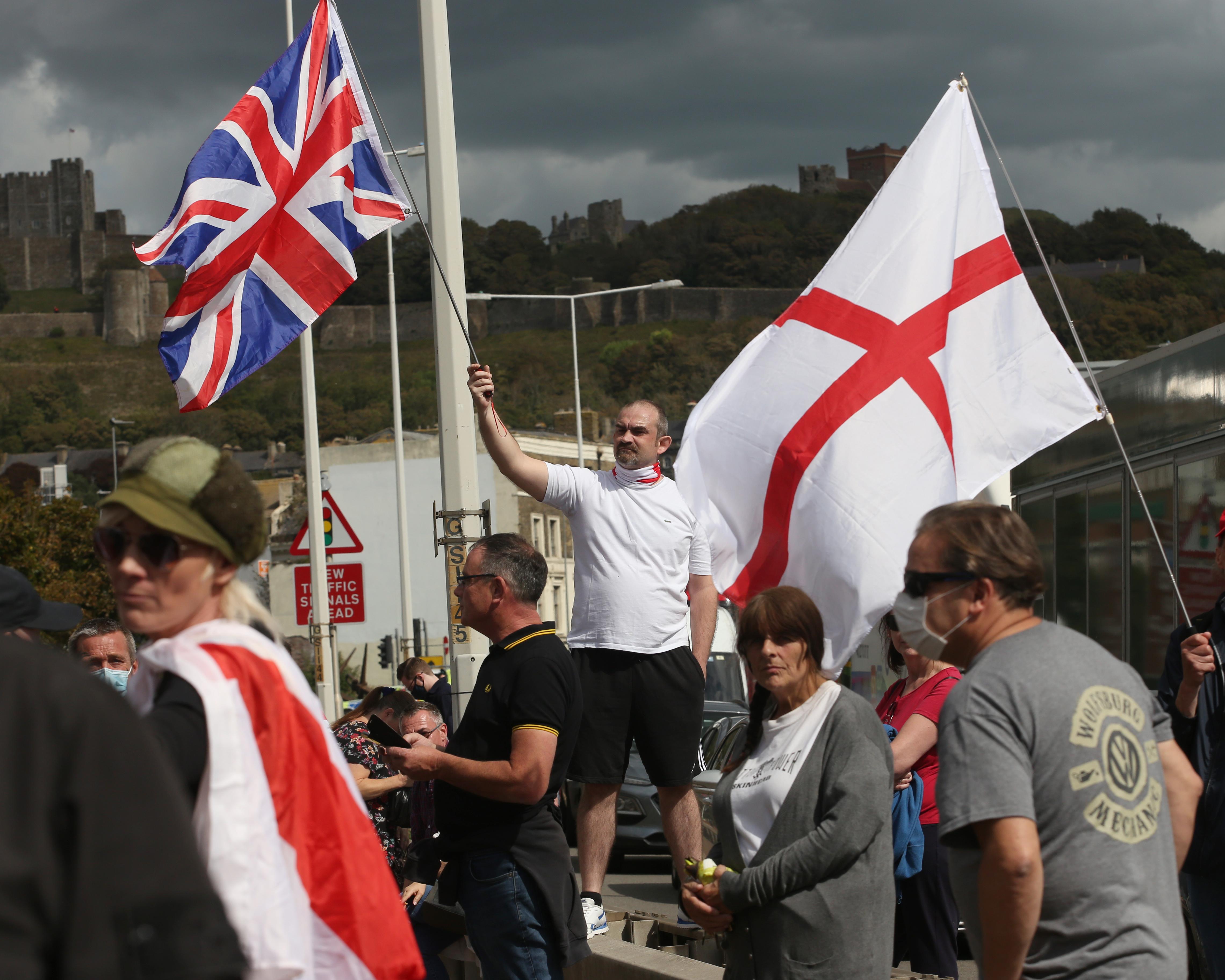 Crowd carrying Union Jack and St George’s flags near a castle beneath dark storm clouds