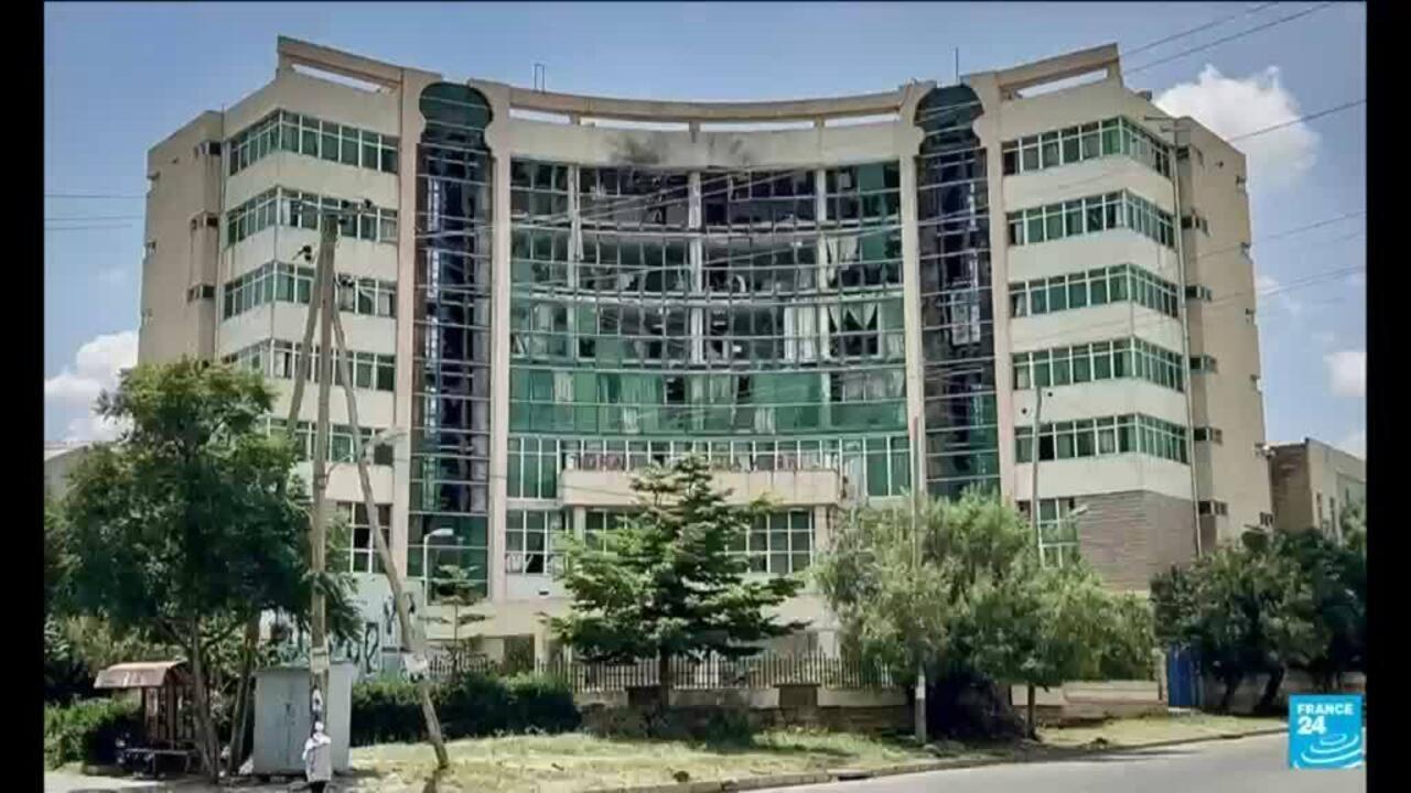 A curved multi-storey office building with extensive glass windows stands behind trees beside a road.