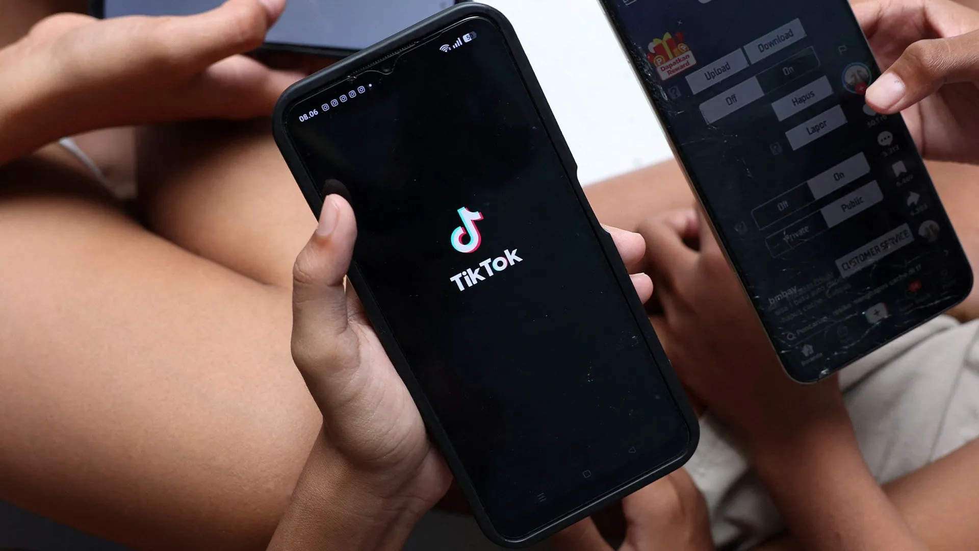 Hands hold smartphones, one displaying the TikTok logo and another showing a video-sharing app interface.
