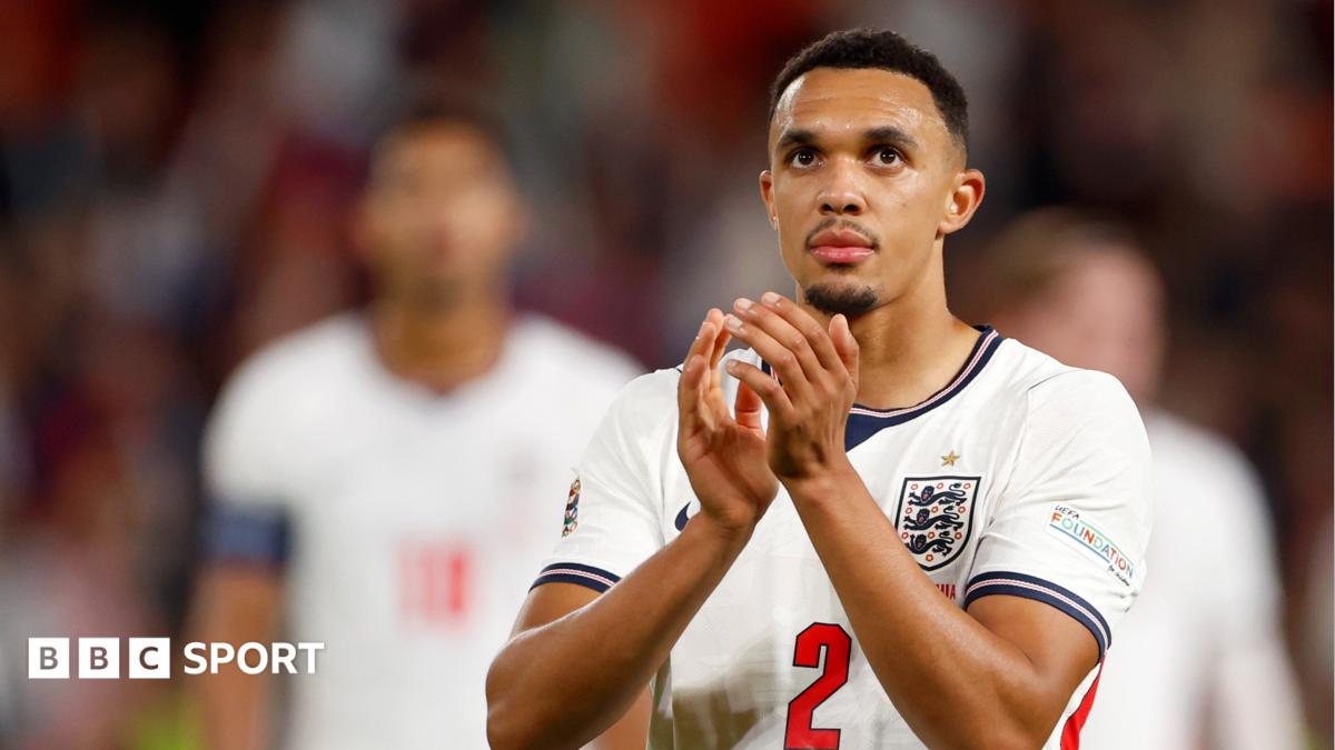 England player in a white kit applauds, with a blurred teammate behind him.
