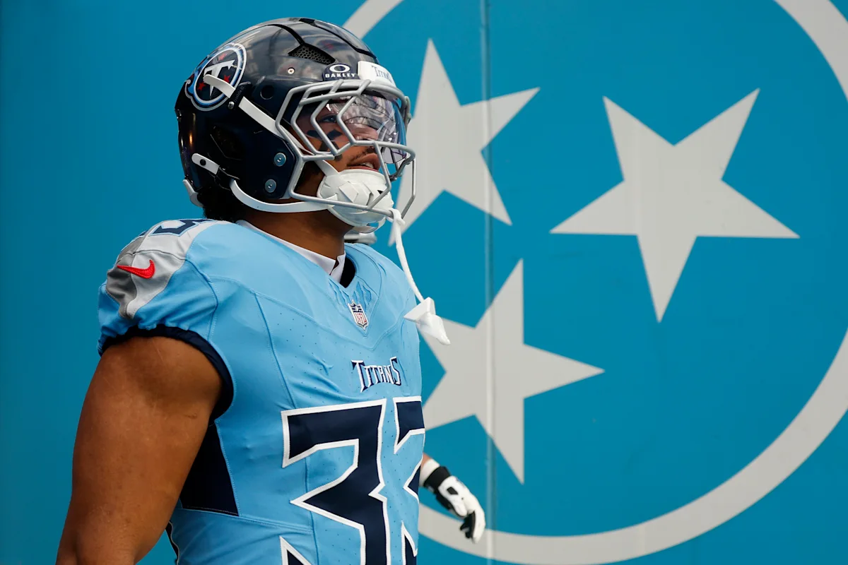 Tennessee Titans football player wearing helmet and light blue jersey stands before a team logo.