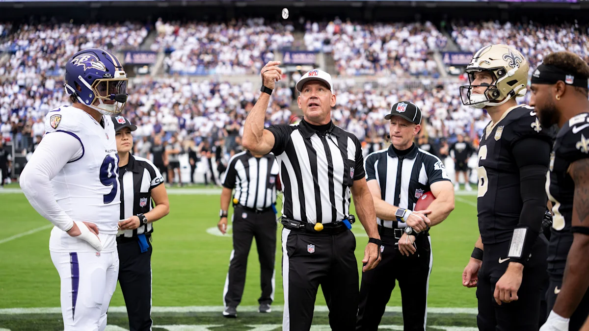 A referee gestures during an NFL game as Ravens and Saints players watch nearby.
