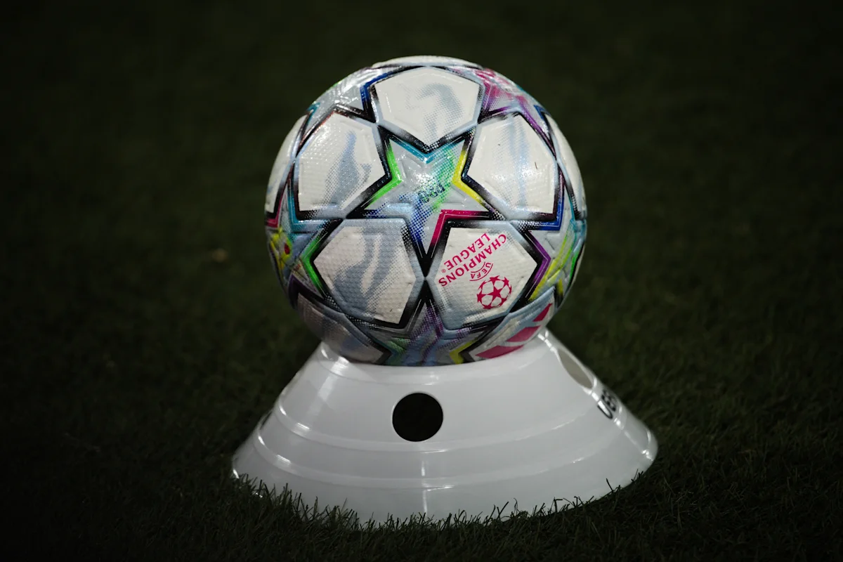 A Champions League football rests on a white display stand on a grass pitch.