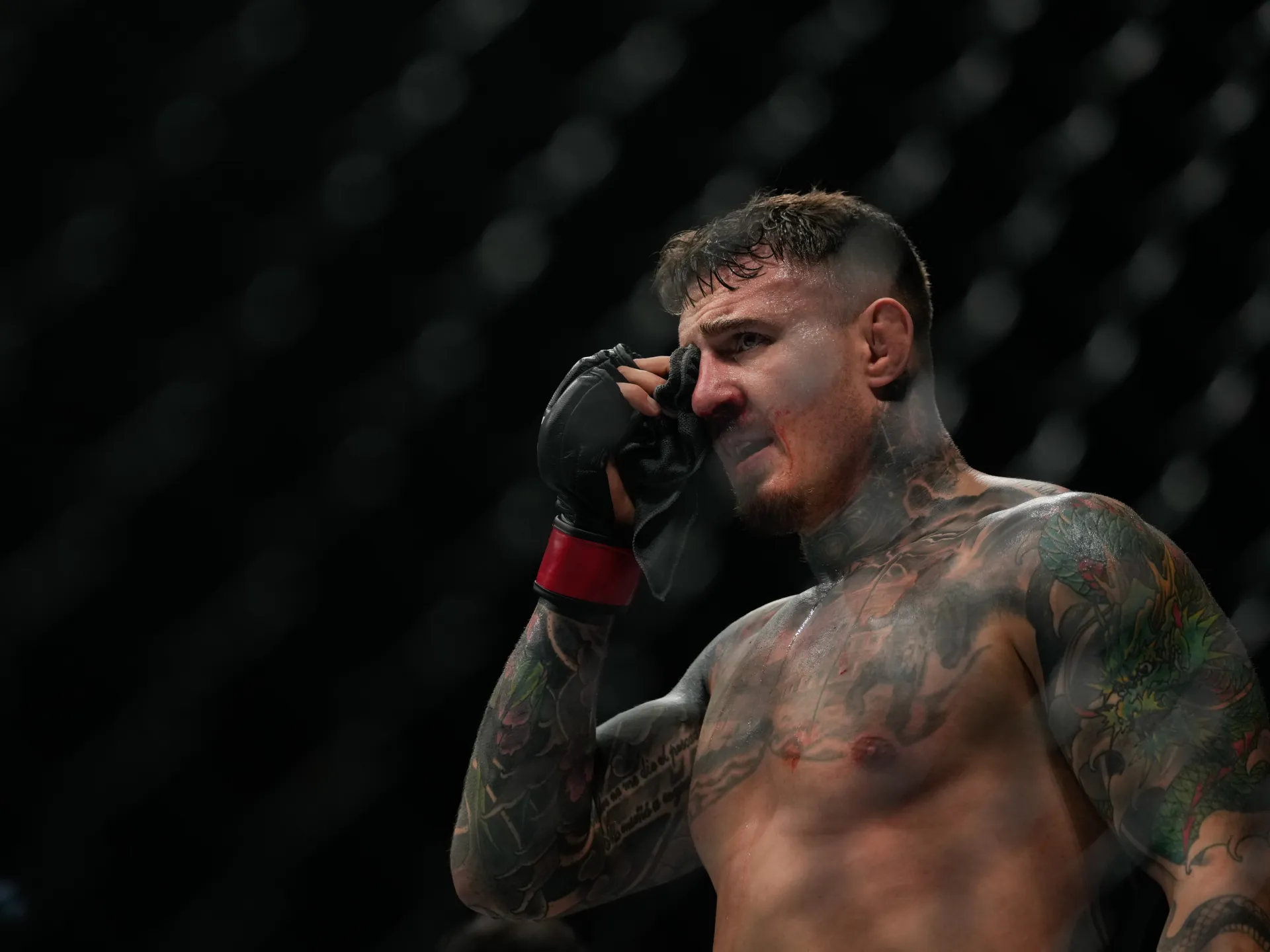 Tattooed fighter presses a towel to his injured eye inside a dim arena.
