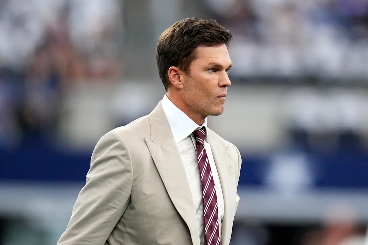 Man in cream suit and burgundy striped tie standing on the sideline during a football game