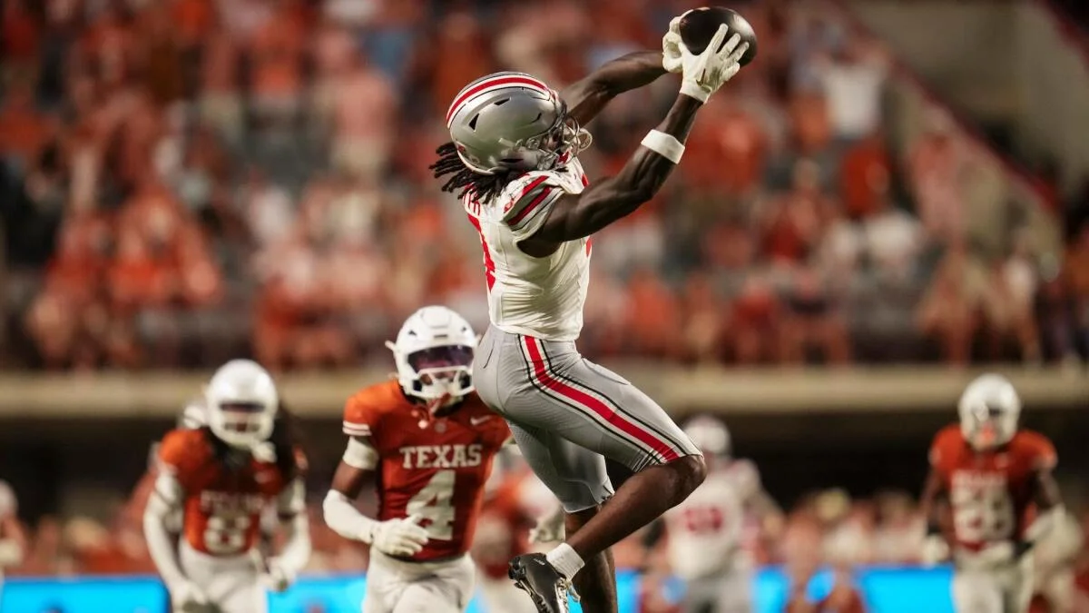 Ohio State receiver reaches to catch a football above Texas defenders during a college football game
