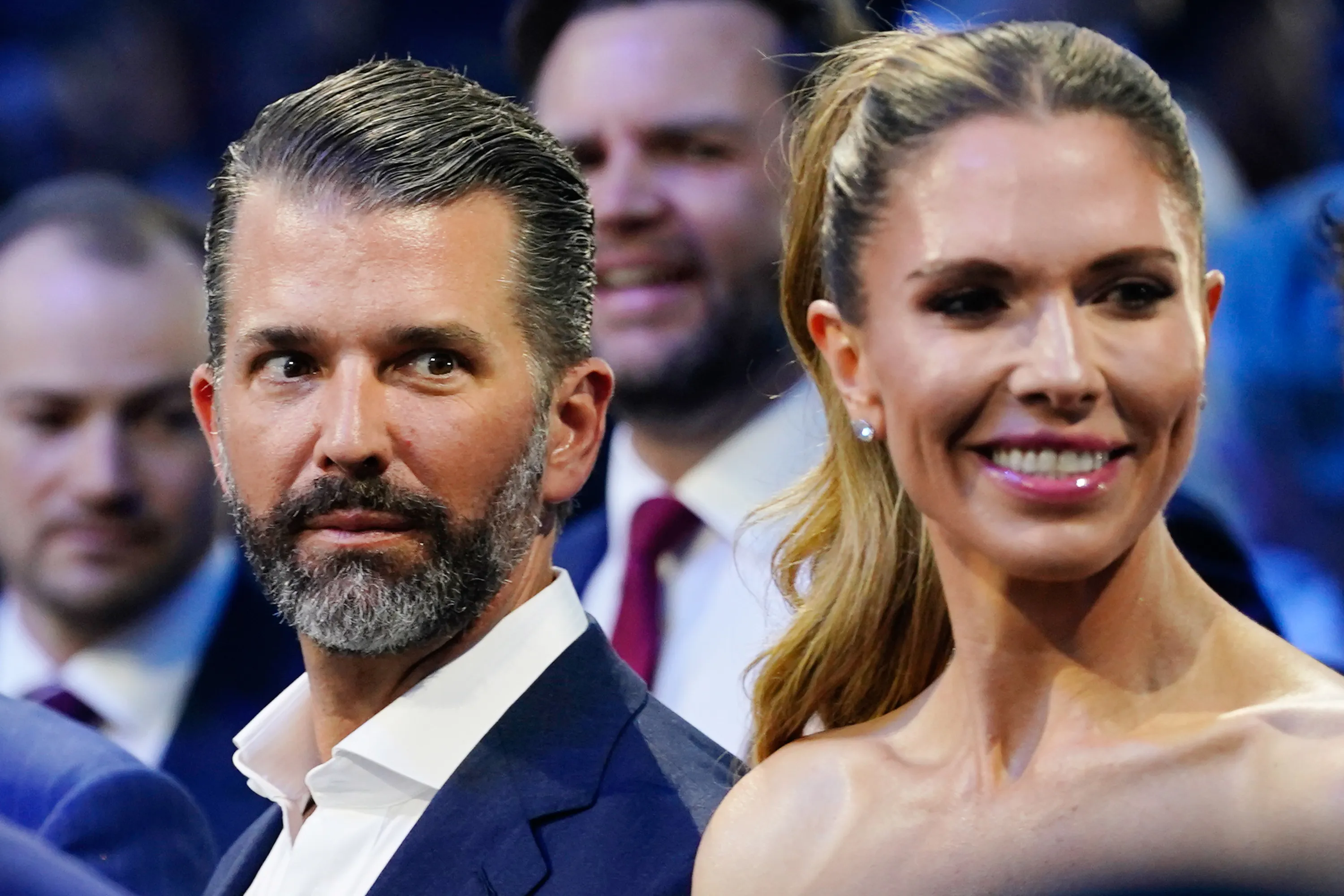 Man with beard and woman with ponytail smile at a formal event amid seated attendees.