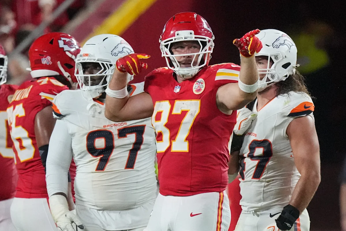 Kansas City Chiefs player Travis Kelce, wearing No. 87, gestures between Denver Broncos players.