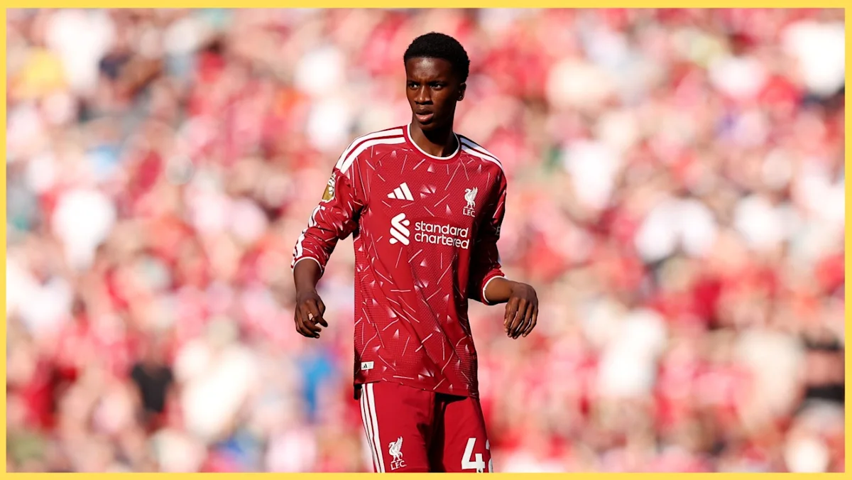Young footballer in a red Liverpool jersey runs on the pitch before a blurred crowd