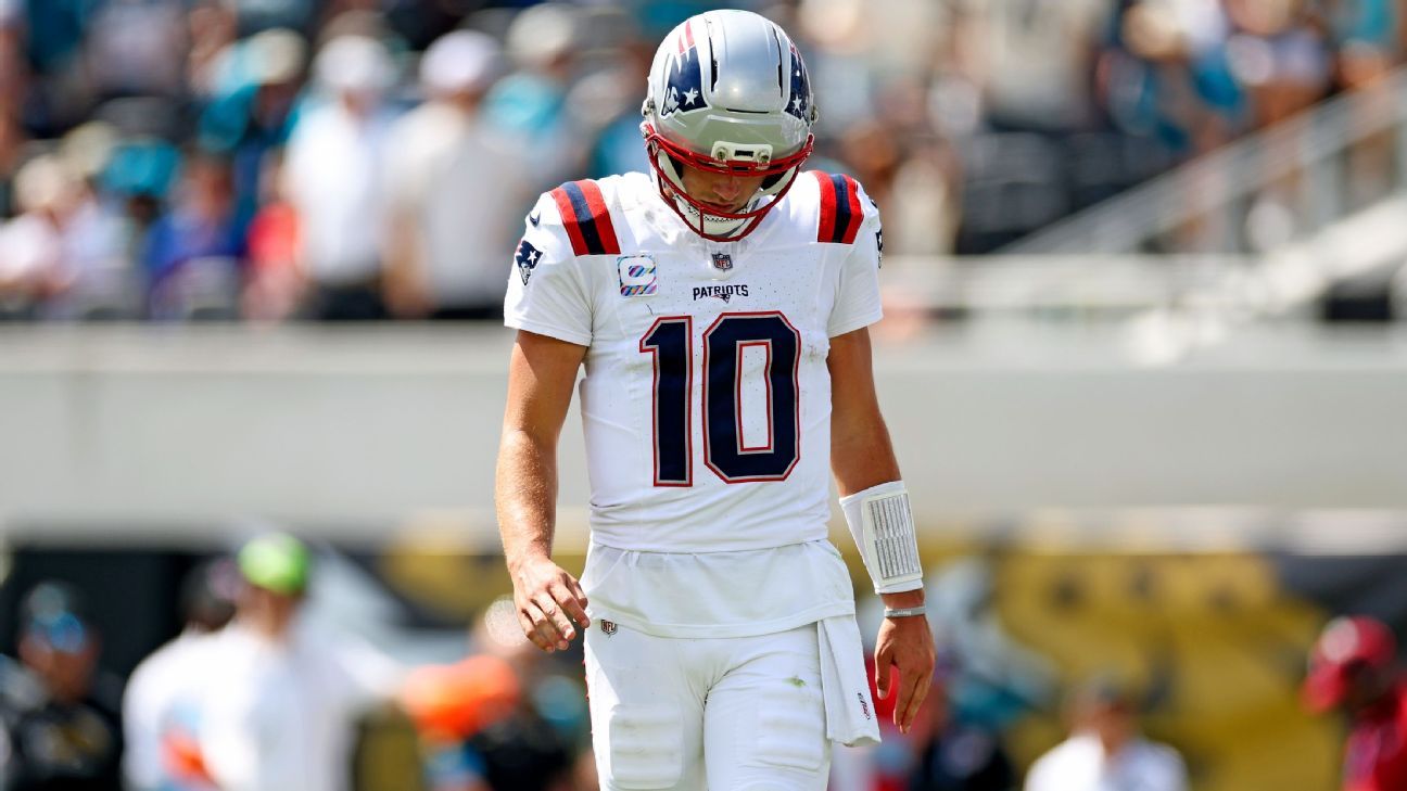 A Patriots player wearing number 10 walks with his head lowered on the field.