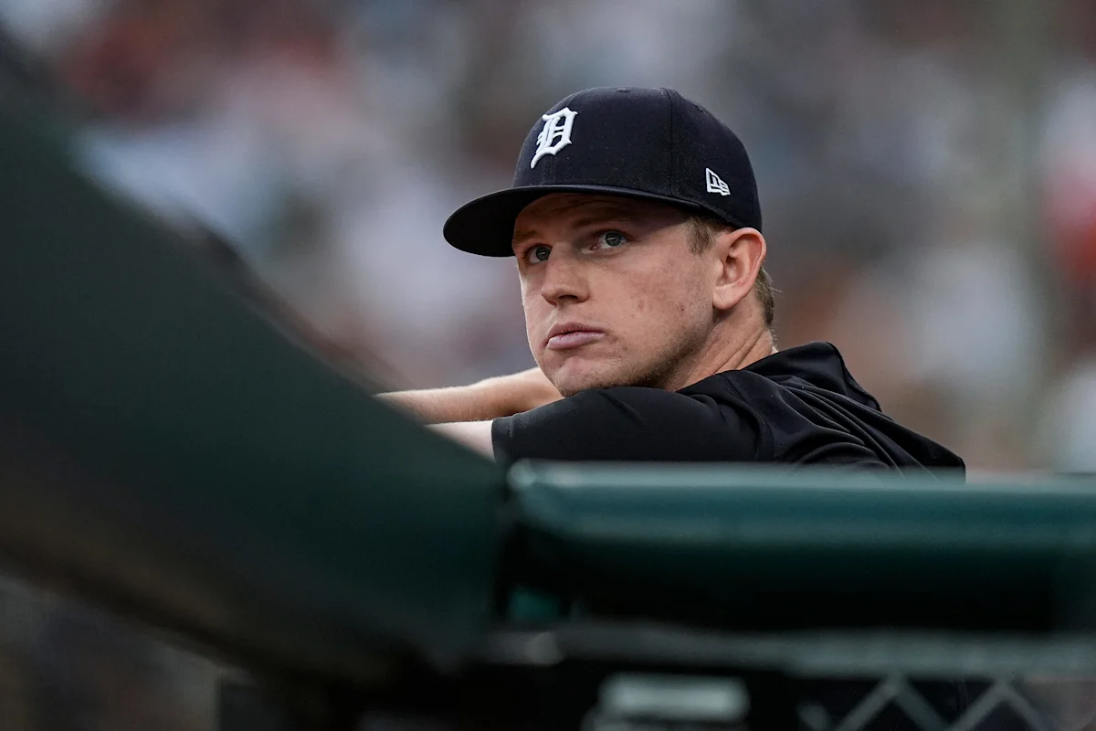 A Detroit Tigers player in a black cap leans on the dugout railing.