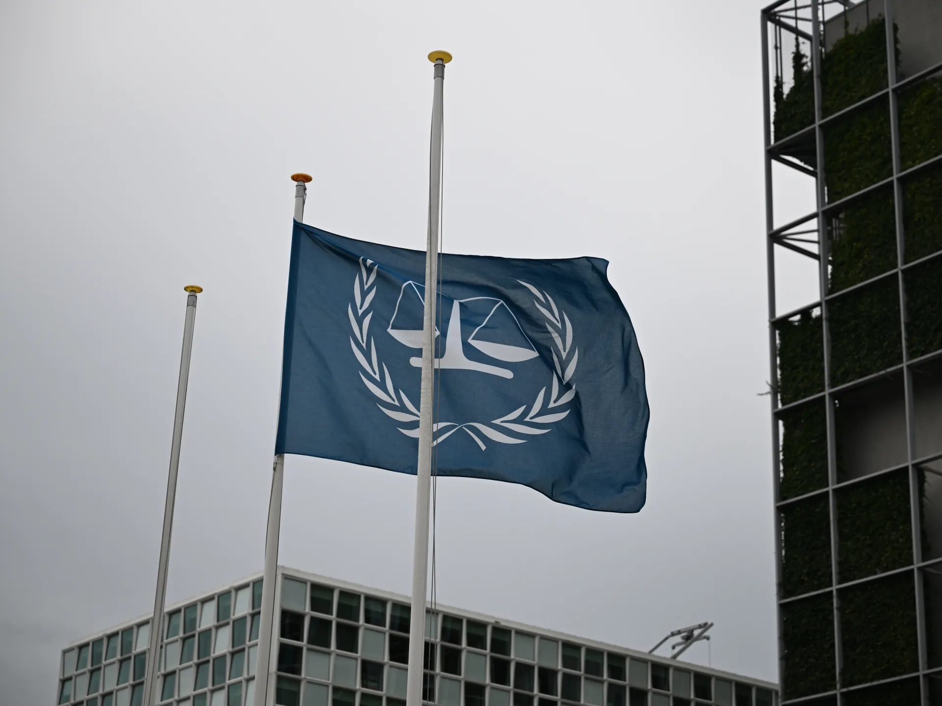 International Criminal Court flag flies beside modern office buildings under an overcast sky.