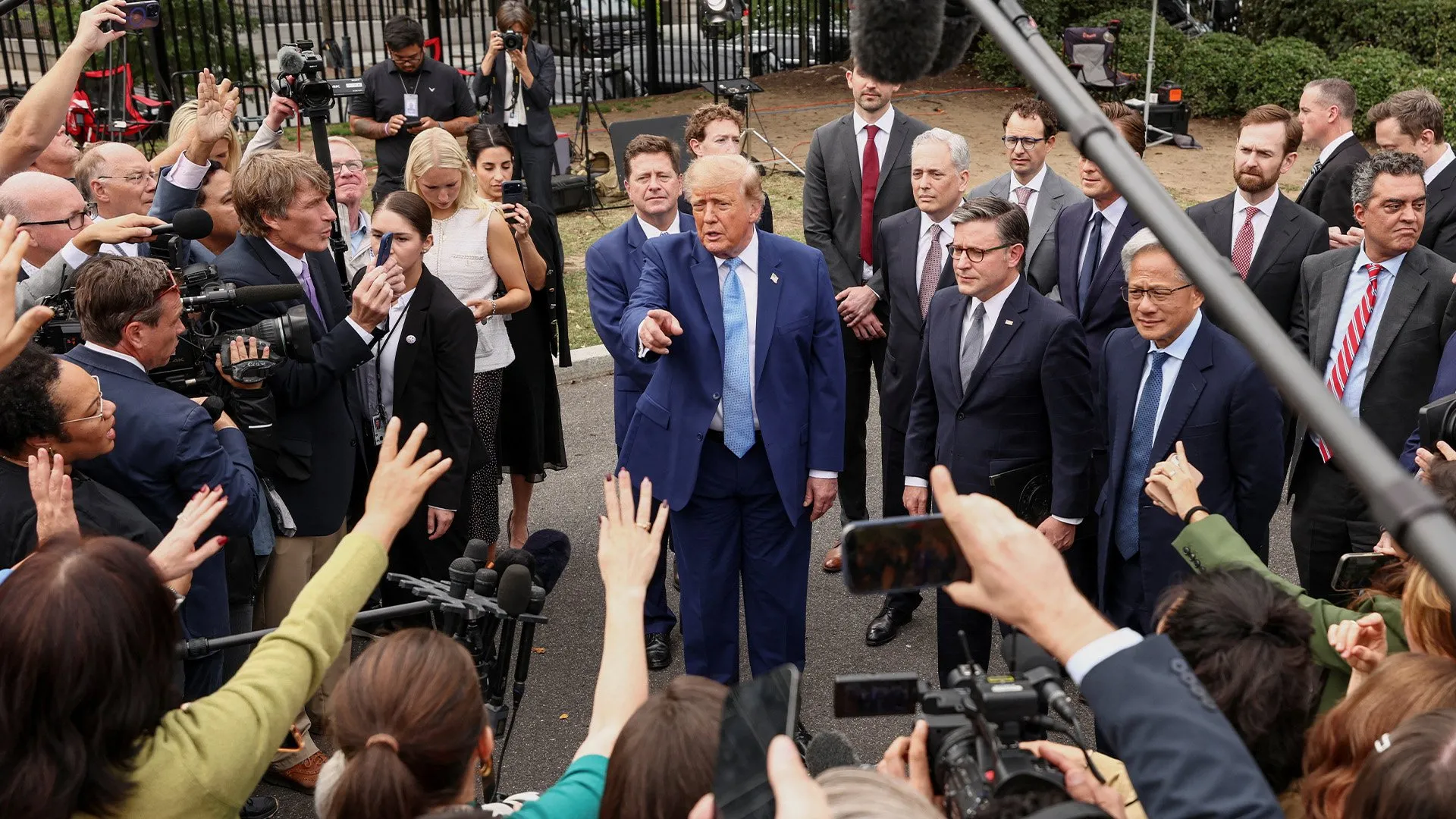 Donald Trump speaks to reporters amid journalists, cameras, microphones, and officials gathered around him outdoors.