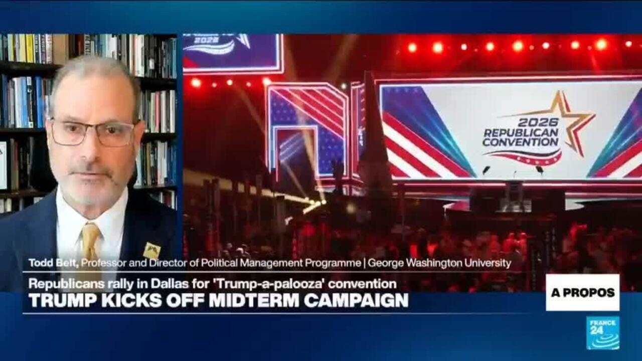 Analyst appears beside a Republican convention stage displaying campaign graphics and the 2026 convention logo.