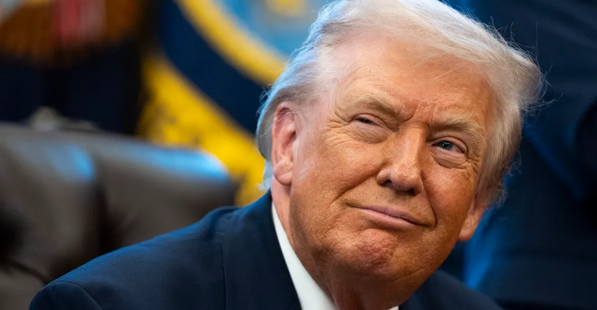 Donald Trump in a dark suit, seated and looking to the side against a blurred background.