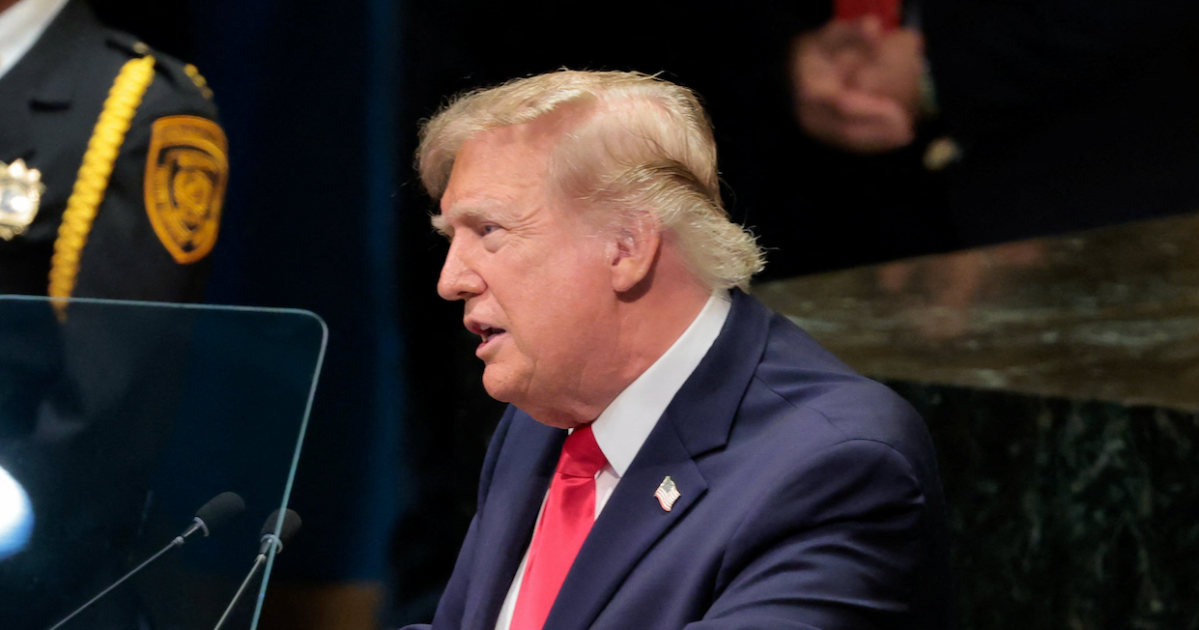 Donald Trump speaks beside a teleprompter at a lectern, wearing a dark suit and red tie.