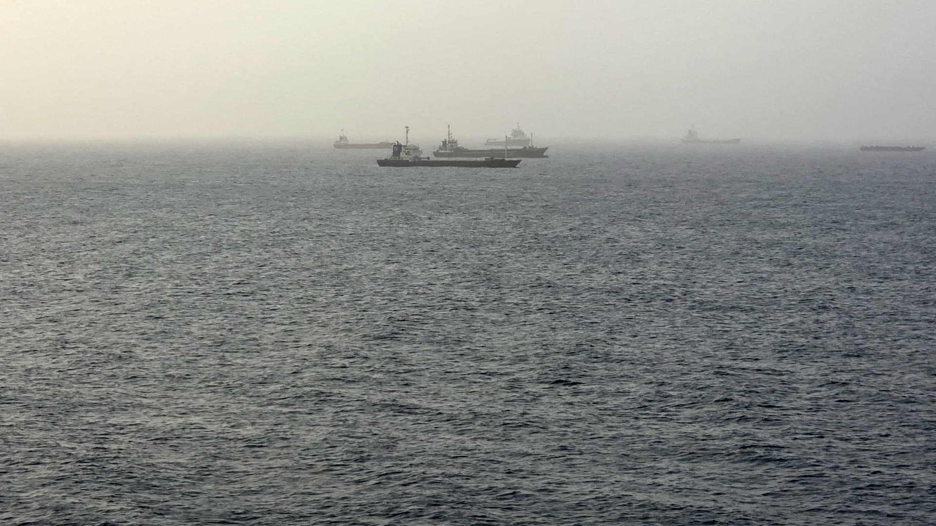 Several cargo ships are faintly visible through fog on a gray, choppy sea.