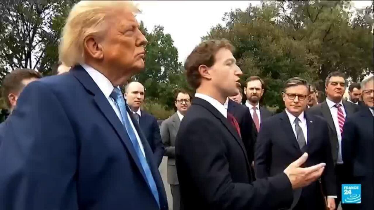 A suited man gestures while speaking to Donald Trump and several officials outdoors.