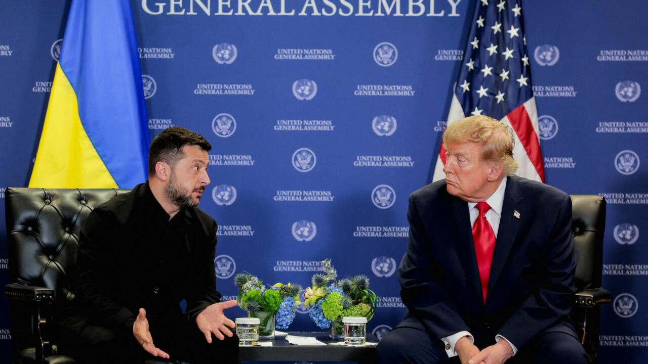 Two men sit facing each other in armchairs beside Ukrainian and American flags.