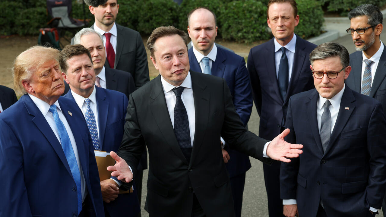 A group of suited men stand together outdoors, with one man gesturing as others look on.