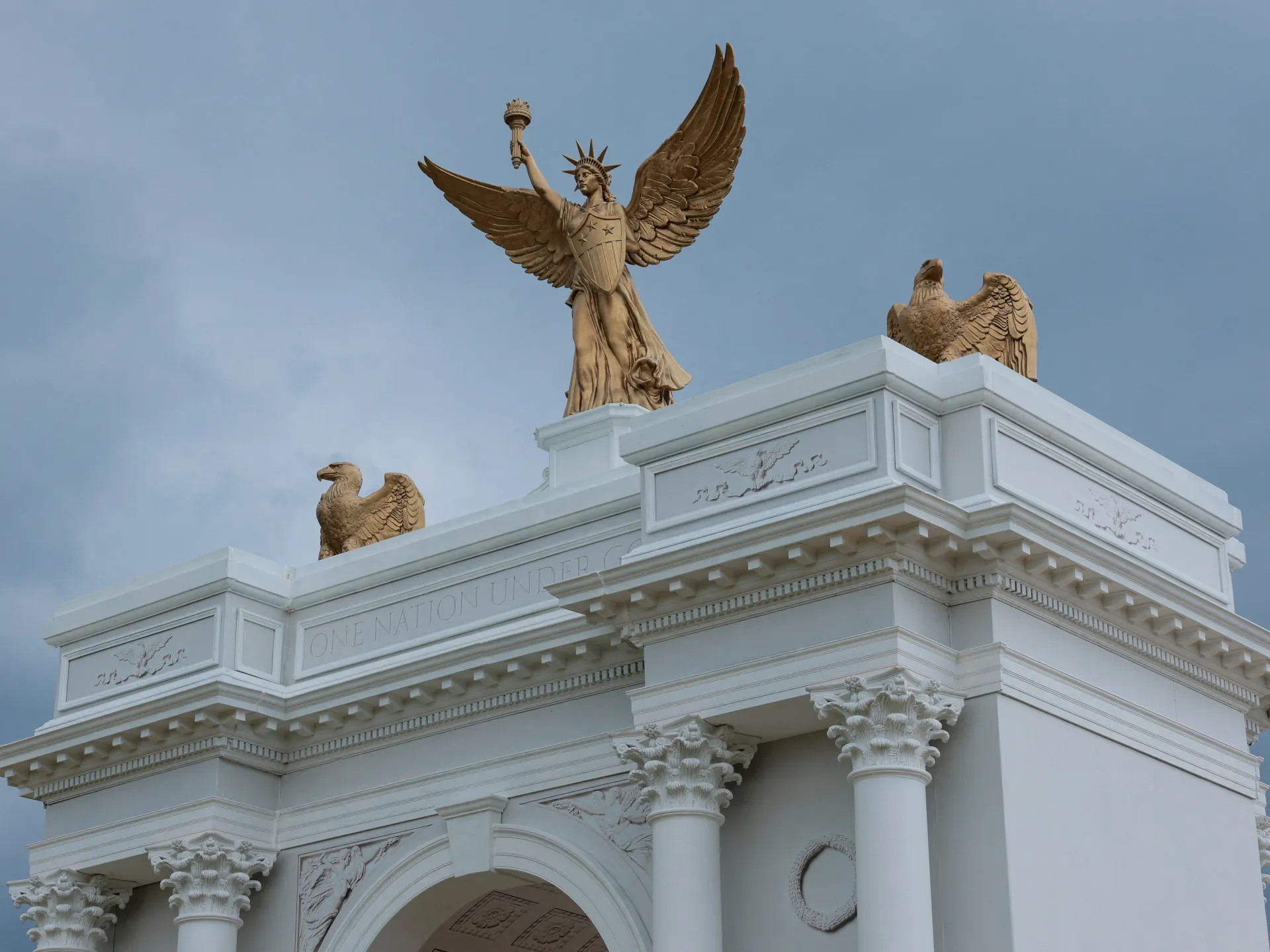 White monumental arch topped by a winged female figure and sculpted eagles beneath a blue sky.
