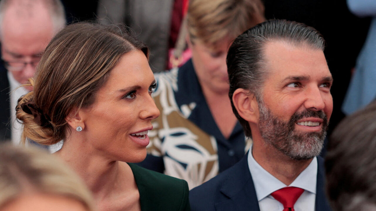 Smiling woman and bearded man in formal attire sit among a crowded group of people.